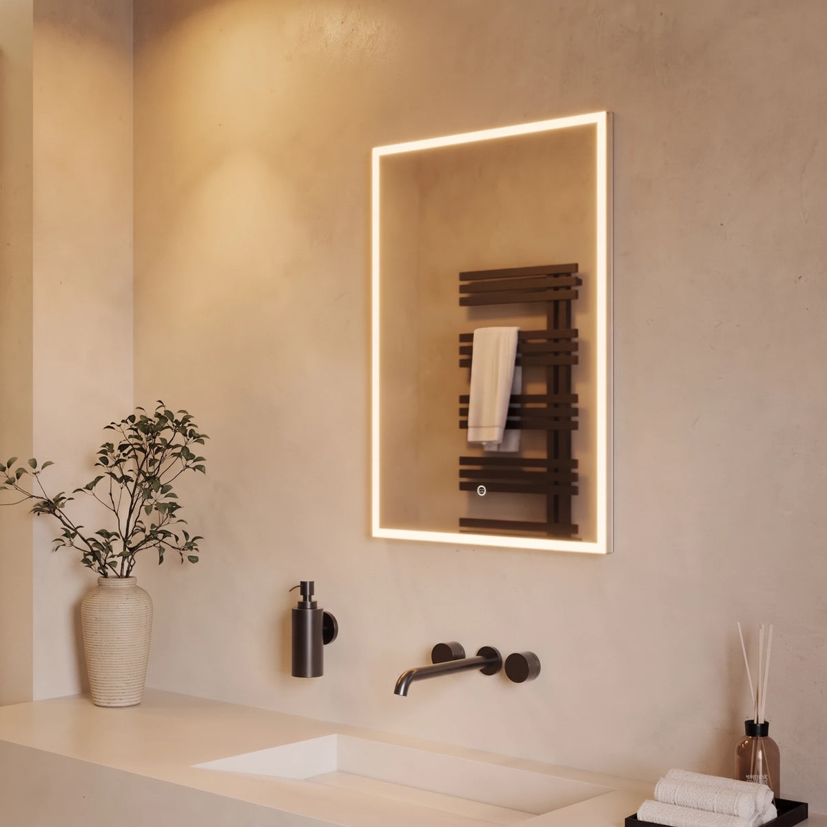 A modern rectangular LED-backlit mirror mounted on a beige plaster bathroom wall above a sink. The mirror reflects a dark wood heated towel rail with a white towel. #Size_500mm x 700mm