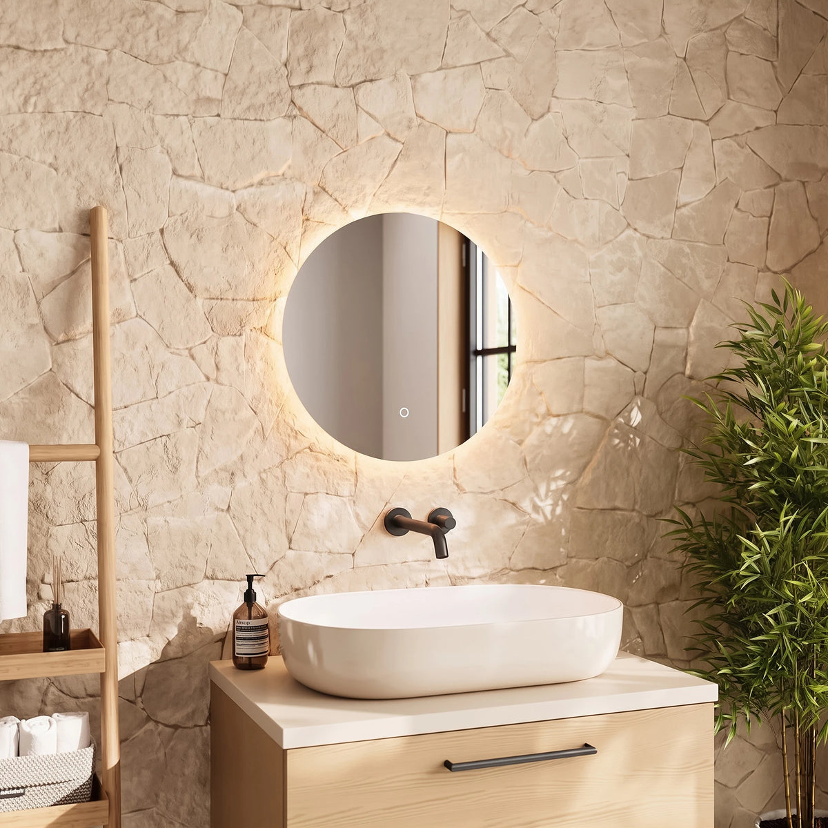 A modern bathroom vanity setup featuring a round backlit LED mirror mounted on a textured stone wall above a light wood cabinet with a white vessel sink. A wooden towel ladder and a green potted plant are visible in the styled room. #Size_⌀500mm