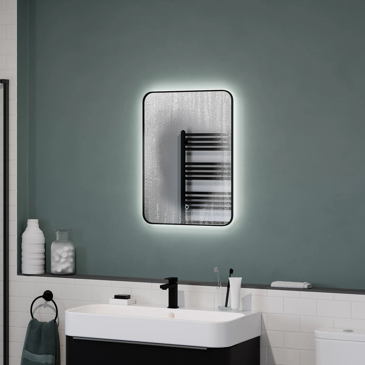 A rectangular wall mirror with a black frame and integrated LED lighting, mounted on a dark green bathroom wall above a white sink and black vanity. #Finish_Black