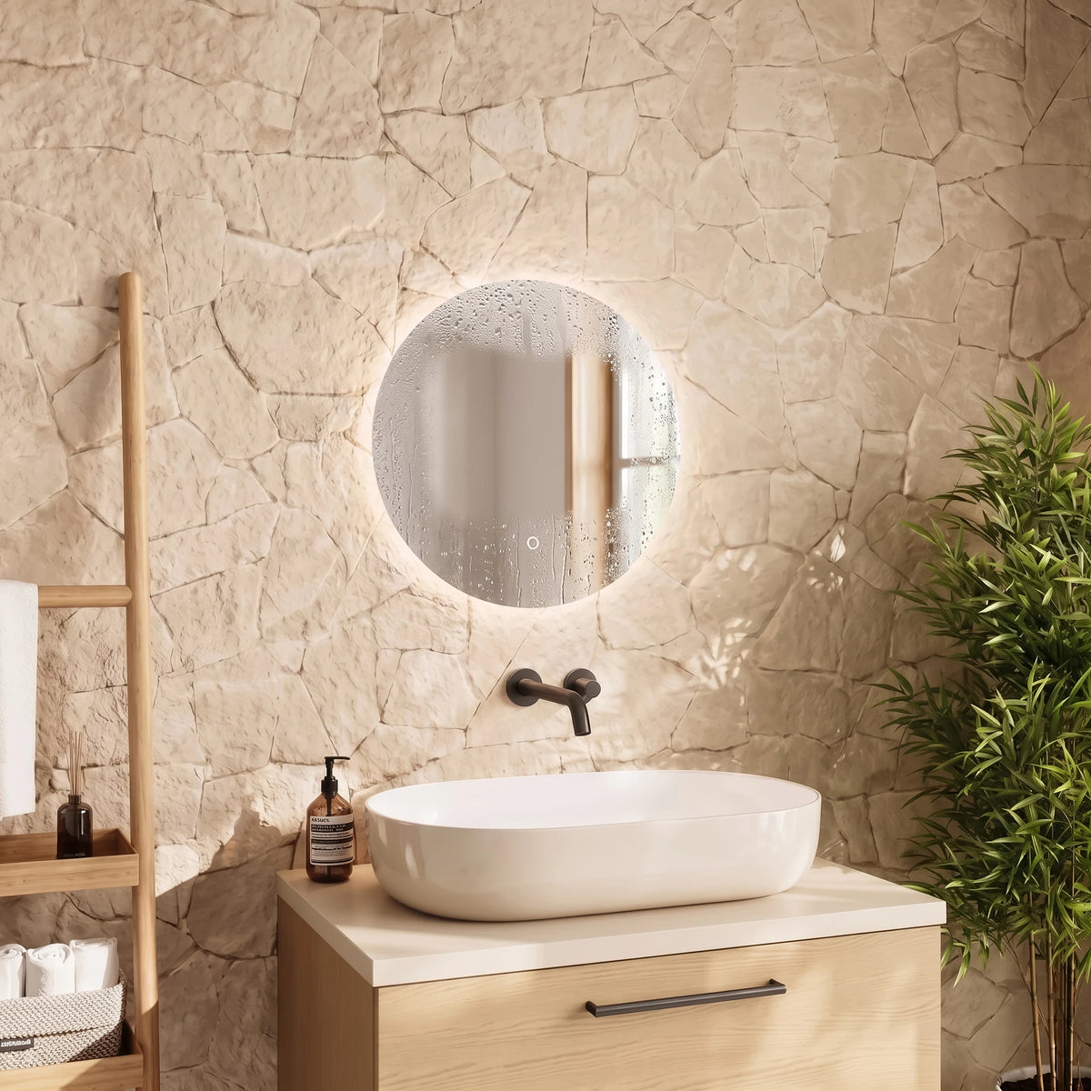 A modern bathroom vanity setup featuring a round backlit LED mirror mounted on a textured beige stone wall above a light wood cabinet with a white vessel sink. A dark bronze faucet and matte black handles are visible, with a wooden shelf ladder and a green potted plant in the background. #Size_⌀500mm