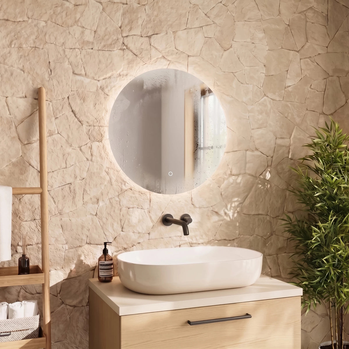 A round LED-backlit bathroom mirror mounted on a textured stone wall above a light wood vanity with a white vessel sink, black faucet, and a bamboo plant nearby. #Size_⌀600mm