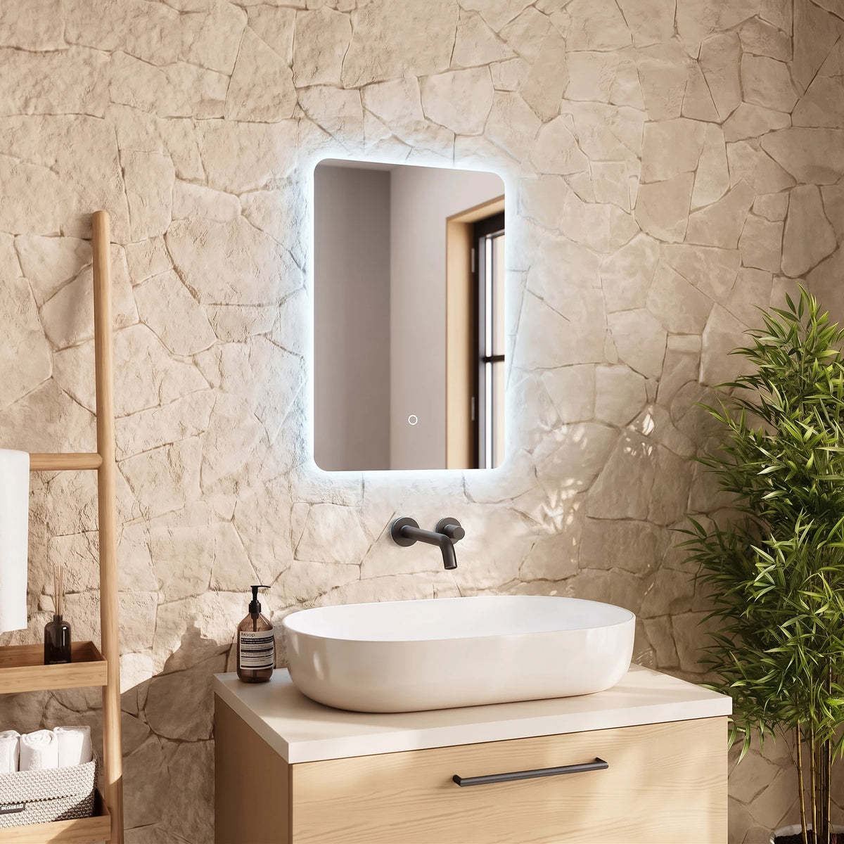 An illuminated rectangular bathroom mirror mounted on a textured stone wall above a white vessel sink and light wood vanity, with a wooden shelf and green plant nearby. #Size_400mm x 600mm