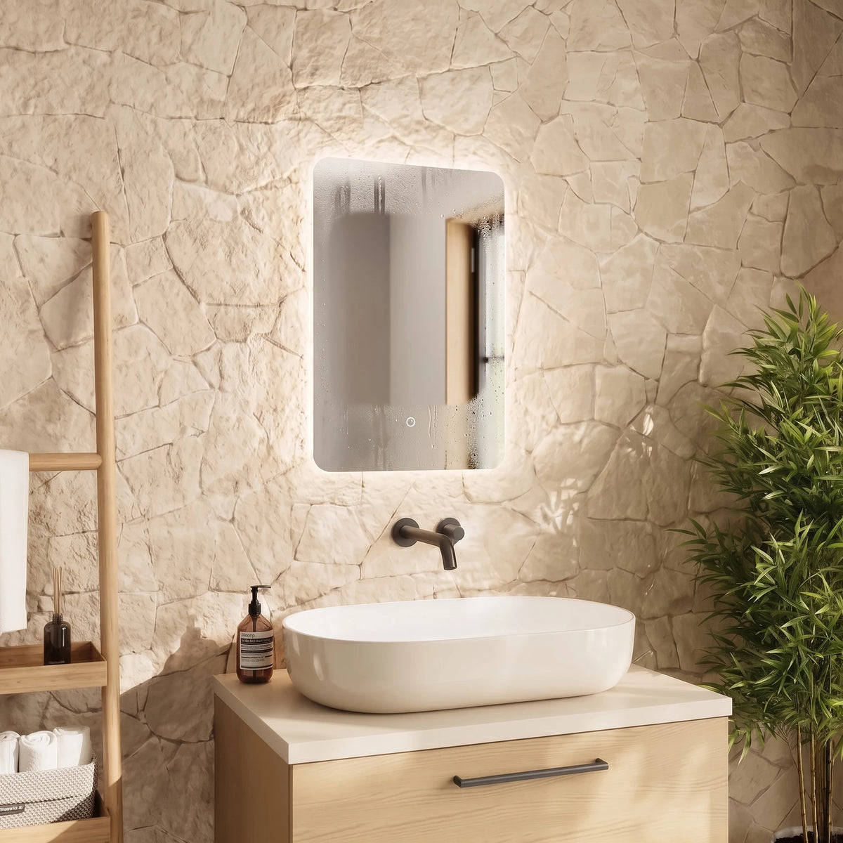 A modern bathroom vanity setup featuring a white oval vessel sink on a light wood cabinet, set against a textured beige stone wall with an illuminated rectangular mirror above. A wooden towel ladder and a green potted plant are visible in the styled room. #Size_400mm x 600mm