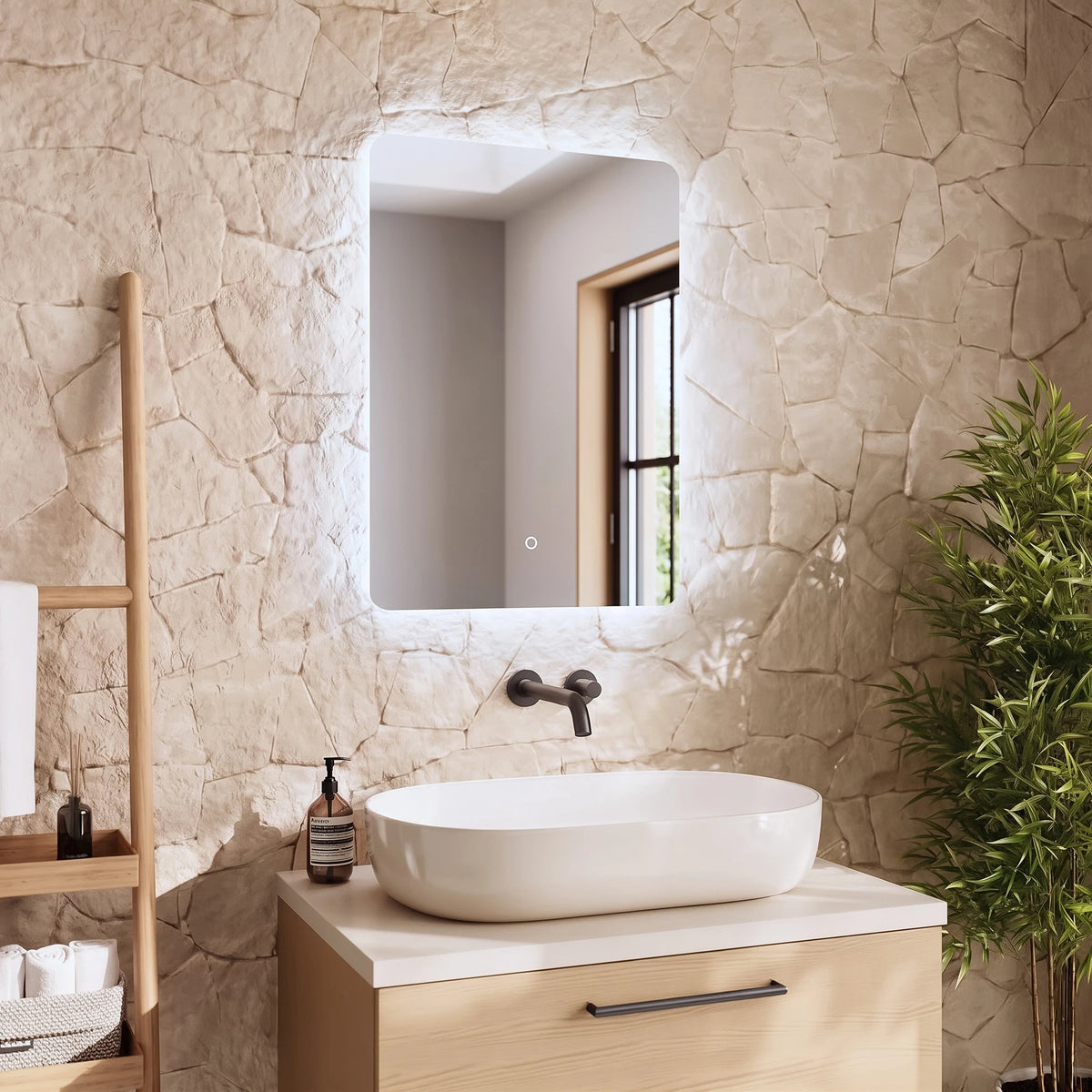 A modern bathroom vanity setup featuring a rectangular backlit LED mirror mounted on a textured beige stone wall. Below the mirror is a white vessel sink sitting on a light wood vanity cabinet with a white countertop. #Size_500mm x 700mm