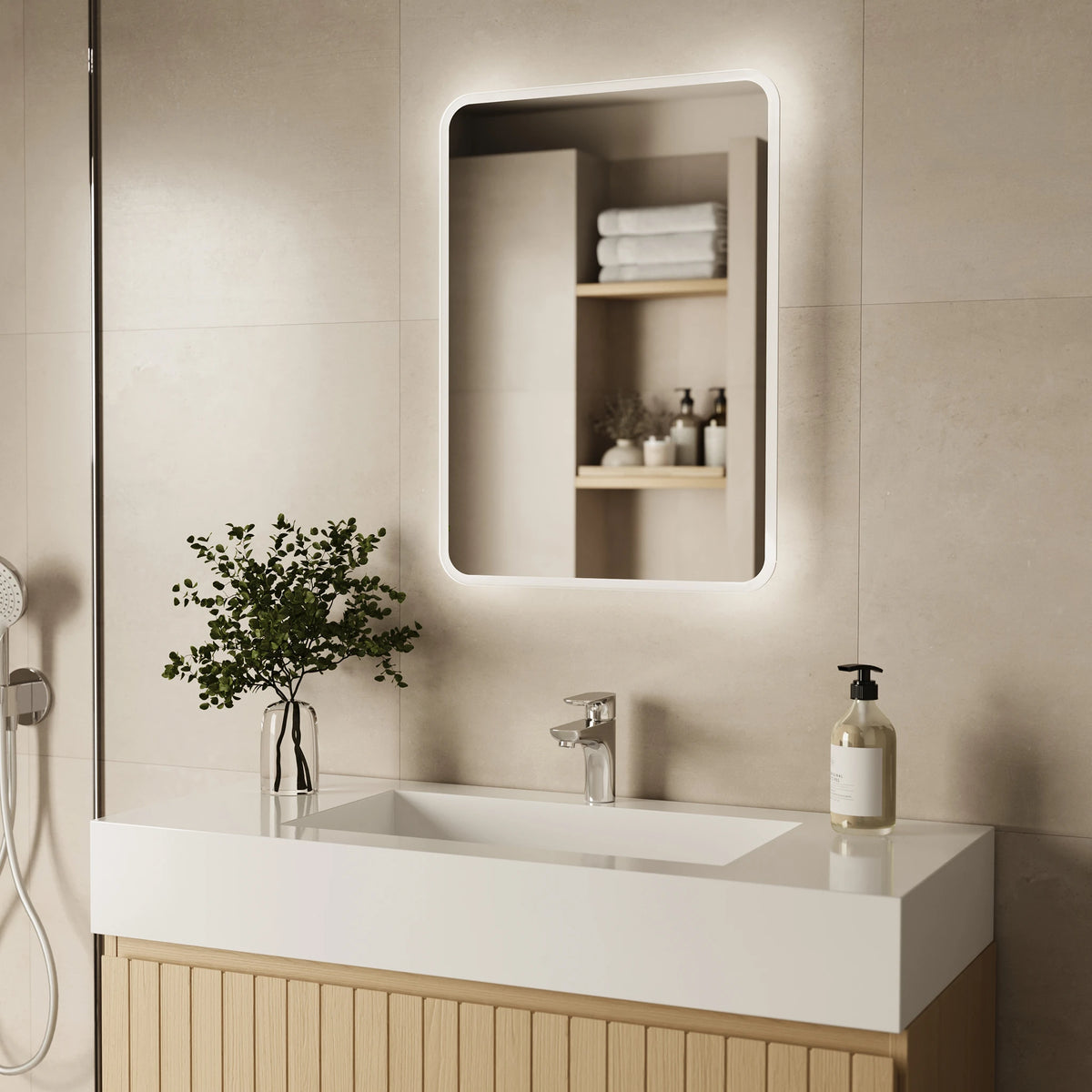A modern bathroom scene featuring a rectangular LED-backlit wall mirror mounted above a white sink with a light wood vanity. The mirror reflects built-in shelves with folded towels and toiletries. #Size_500mm x 700mm