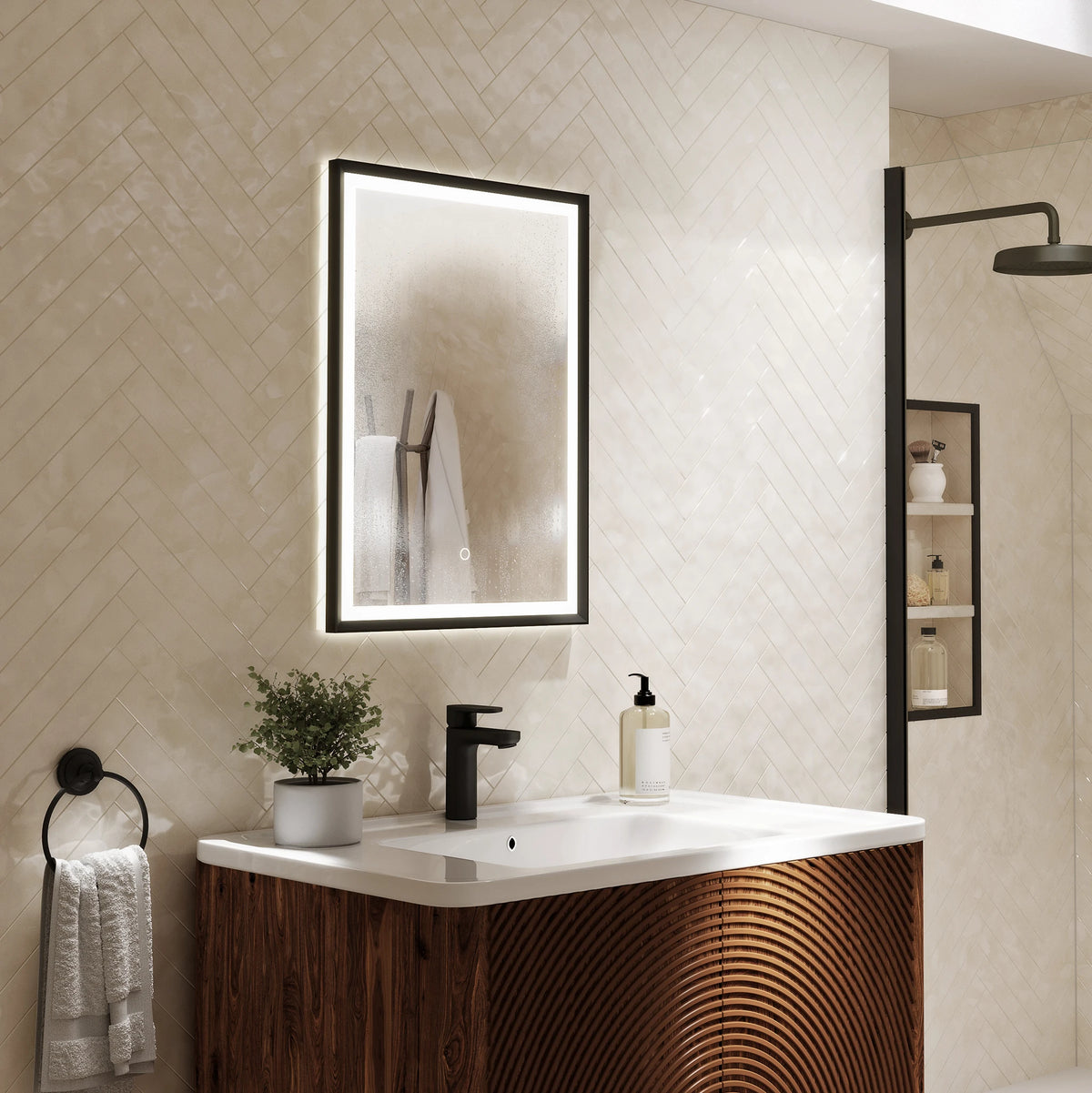 A modern bathroom vanity setup with a rectangular backlit mirror, white sink countertop, black faucet, and a wood-look cabinet with curved front detailing. The wall behind is covered in light beige diamond-pattern tile, and a shower area is visible to the right. #Finish_Black